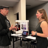 Professional talks to GVSU student in front of her table.